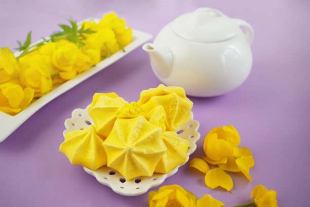 黄色蛋白霜放在心形盘子里。蛋白霜和黄花的静物画，茶壶和茶图片下载