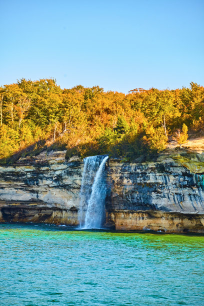 夏季森林后面高大的瀑布流入湖泊或海洋与图片岩石在国家公园图片下载