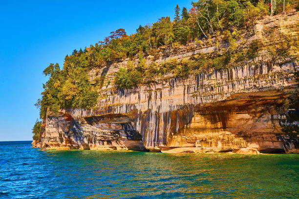照片中岩石的阳面，灌木和树木生长在湖上的悬崖上图片下载