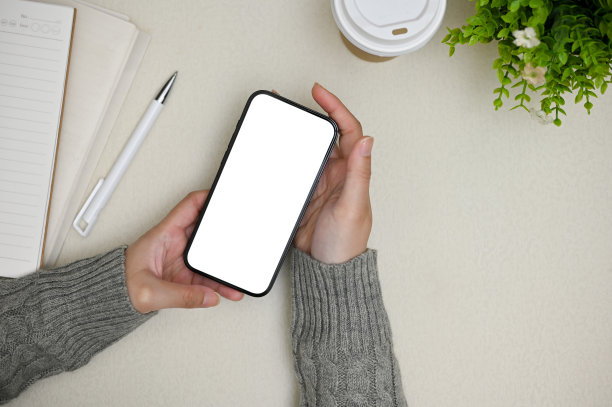 俯视图，一名女性手持智能手机模型站在灰色办公桌前。图片下载