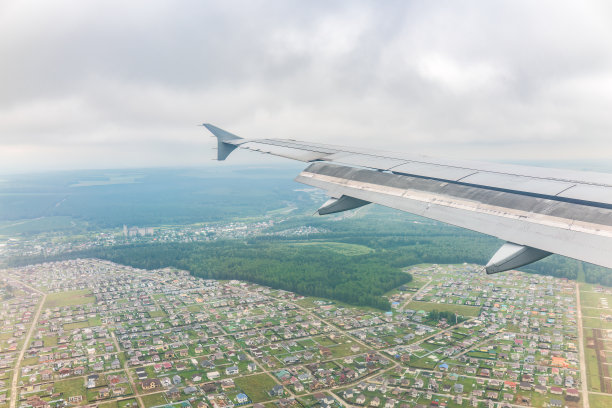 飞机机翼的视图，蓝天和绿色的土地在着陆。飞机窗口视图。图片下载
