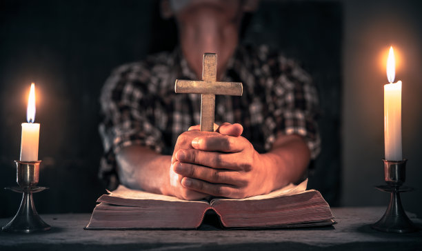 年轻男性在敬拜室拿着十字架在木桌上祷告。基督教的概念。图片下载