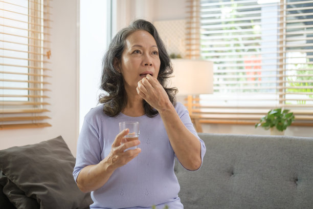 健康的老年妇女手持一杯水，每天服用药片以保持健康。用药、治疗和保健理念。图片下载