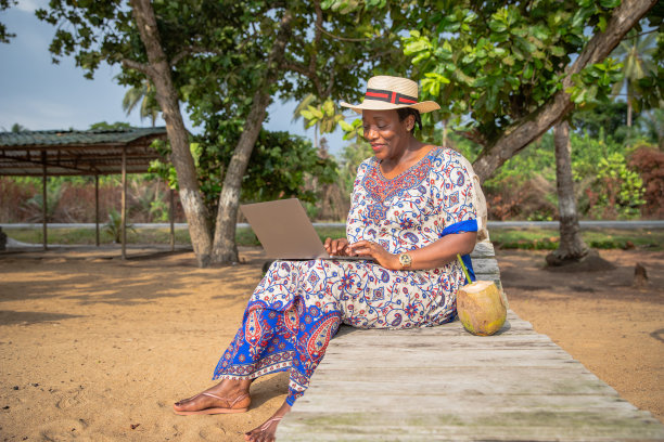 一个成熟的女人坐在沙滩上的躺椅上用笔记本电脑工作图片下载