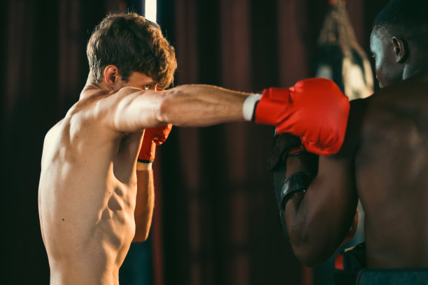 在健身房进行拳击搏击健身训练，配有私人教练和陪练垫。健康动机和肌肉锻炼，拳击手抛出一拳，并在综合格斗工作室运动手套锻炼。图片下载