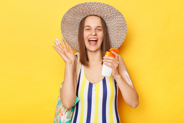 漂亮快乐的女人穿着泳装，在黄色背景上显示spf霜在照顾她的皮肤，兴奋地尖叫着防紫外线。图片下载