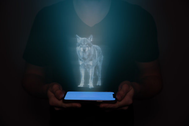 一个来自未来的年轻人拿着一个智能手机，上面投射着一只狼。未来的技术。图片下载