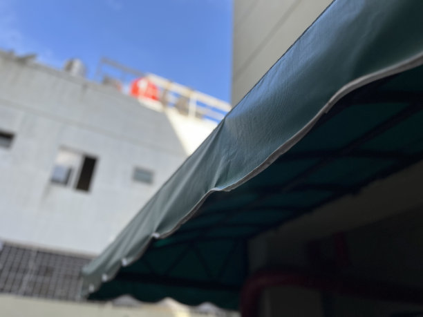 在炎热的阳光明媚的日子里，蓝天和高层建筑的圆形绿色咖啡馆或酒店商业顶篷的特写图片下载