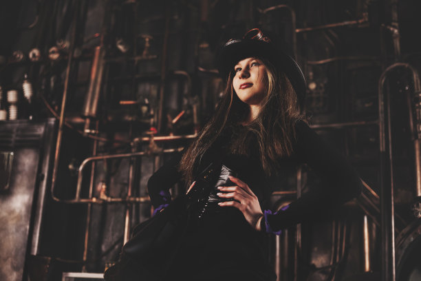 13-14岁的时尚少女模特的肖像，蒸汽朋克形象，穿着黑色连衣裙，看着别处。十几岁的女演员在工业室内摆姿势的照片。冒险的概念。复制广告文本空间图片下载