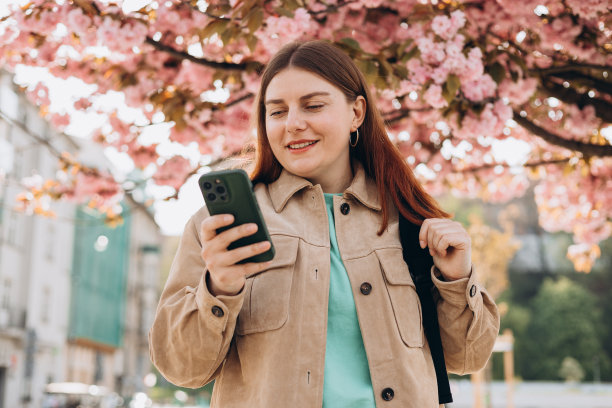 美丽时尚的女人走在春天的一天，拿着手机在街道背景。电话沟通。城市生活方式概念。查看社交网络，发短信。图片下载