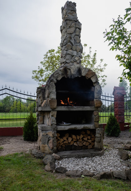 石头烧烤在花园与防火栅栏和植物的背景。图片下载