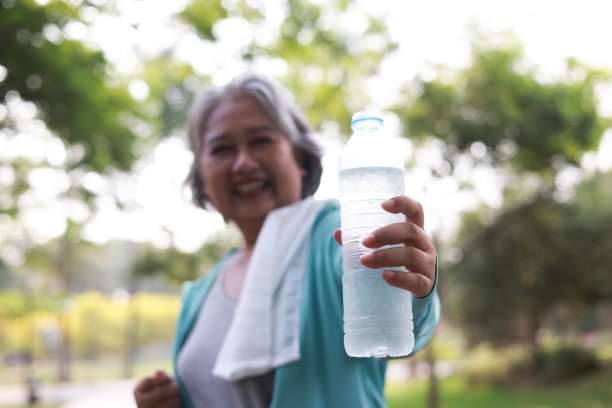 一个快乐、活跃、美丽的老年妇女在户外运动后摆姿势的肖像，运动的老年妇女在公园拿着一瓶水图片下载