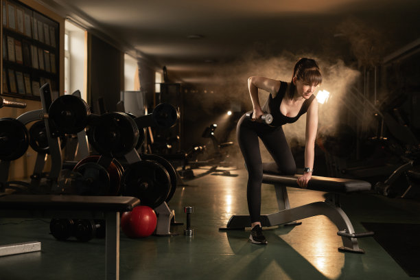 健身女性在健身房里举哑铃跪在板凳上，体现运动、生活方式和健康理念图片下载
