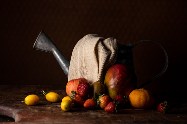 前面的静物照片，上面有水果和水罐，上面有布。图片下载