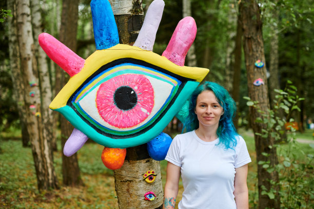 在大眼艺术装置旁，穿着白色T恤，染成蓝绿色头发的微笑年轻成年女子图片下载