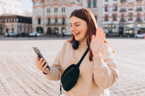 一个快乐的年轻女子走在城市的街道上。女孩在户外用手机和耳机进行视频通话，博主记录了故事图片下载
