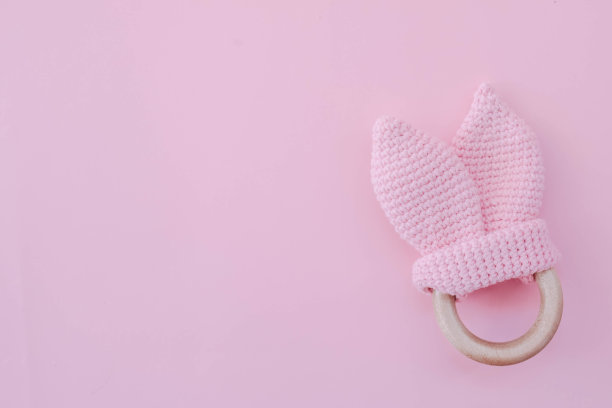 婴儿摇铃玩具。儿童针织兔子在粉红色的背景为一个女孩。给新生儿的手工拨浪鼓。图片下载