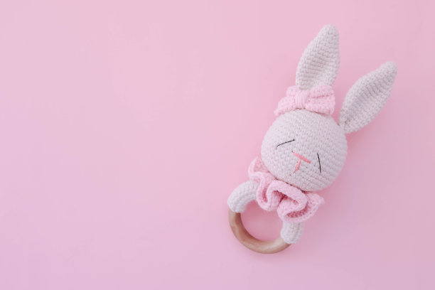 婴儿摇铃玩具。儿童针织兔子在粉红色的背景为一个女孩。给新生儿的手工拨浪鼓。图片下载