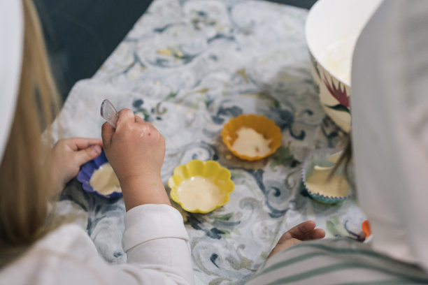 一个女孩的手用勺子舀着刚做好的自制纸杯蛋糕面糊放在塑料包装纸上的特写照片。图片下载