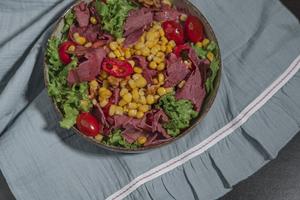 熟食肉冷切与蔬菜，樱桃番茄，甜玉米，核桃和生菜沙拉叶沙拉在厨房纺织品布和深色背景图片下载