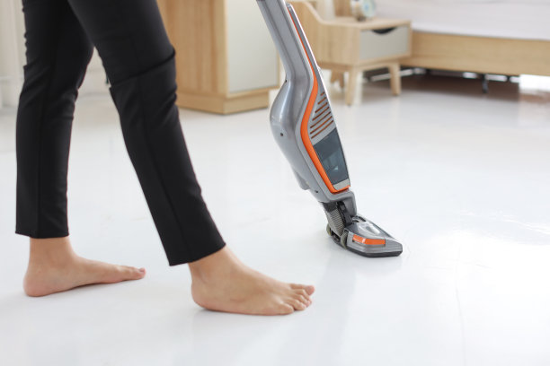 特写活跃的家庭主妇的腿用真空清洁地板与中小企业和电子商务包装箱的背景。穿着黑色打底裤的清洁女孩正在用吸尘器清扫她的房间。室内清洁概念图片下载