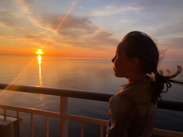 一个7岁的白人女孩的肖像，这个孩子站在船的甲板上欣赏日落。女孩的剪影。图片下载