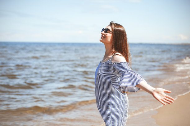 快乐的微笑的女人在自由幸福的海滩上，站在敞开的双手。一位身穿夏装的黑发女模特在户外旅游度假时享受大自然的肖像图片下载