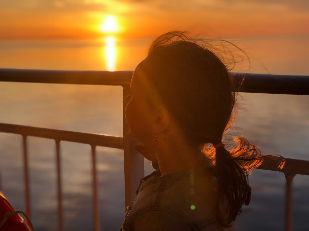 一个7岁的白人女孩的肖像，这个孩子站在船的甲板上欣赏日落。女孩的剪影。图片下载