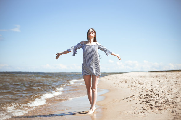 快乐的微笑的女人在自由幸福的海滩上，站在敞开的双手。一个深色头发的女模特在户外旅行度假时穿着夏装享受大自然的肖像，整体计划图片下载