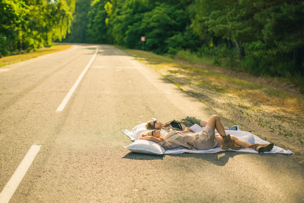公路旅行。两个年轻的金发女孩在森林里的旧公路上玩得很开心。图片下载