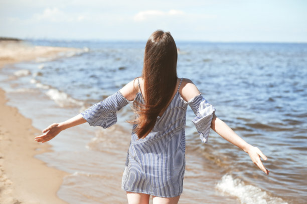 快乐的微笑的女人在自由幸福的海滩上，站在敞开的双手。一位身穿夏装的黑发女模特在户外旅行度假时享受大自然的肖像，背面图片下载