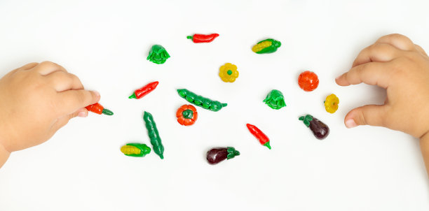 BBanner。宝宝手上玩着橡皮泥蔬菜:玉米、豌豆、茄子、白菜、辣椒。创意手工蔬菜。幼儿的发展。图片下载