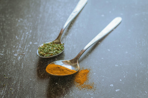 黑色背景上盛有香料和香草的勺子。食品和烹饪材料。图片下载