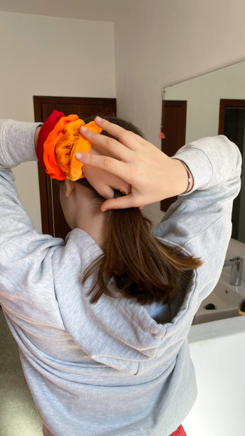 一个十几岁的女孩，手腕上系着红色和橙色的发带，把头发扎成马尾图片下载