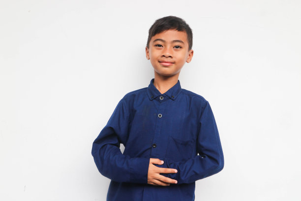 穿着蓝色衬衫的男孩微笑着看着镜头，同时把手放在舒适的肚子上图片下载