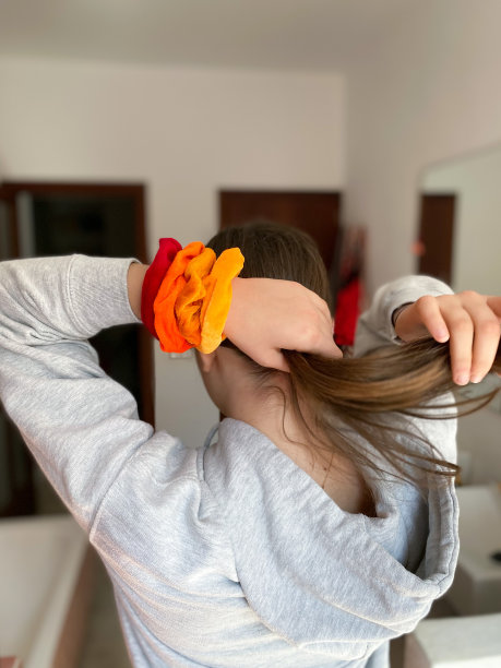 一个十几岁的女孩，手腕上系着红色和橙色的发带，把头发扎成马尾图片下载