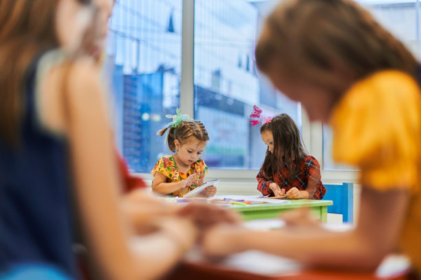 在日托中心的美术课上或小学教室里与女老师一起画画的富有创造力的孩子们。图片下载