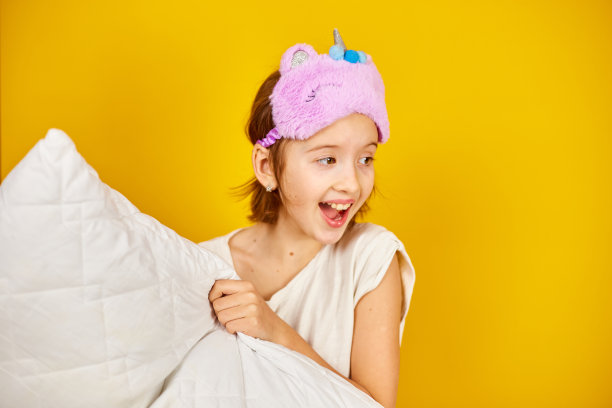 有趣的十几岁的女孩穿着白色睡衣，带着紫色的睡眠面具抱枕头图片下载