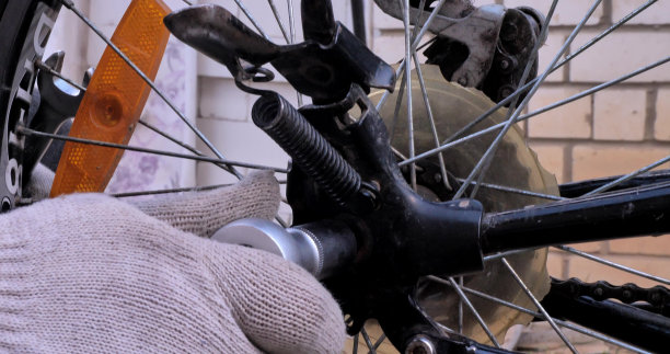 戴着工作手套的手用扳手拧紧自行车车轮上的螺母。特写镜头。一名男子在夏季开始前修理自行车。更换自行车的旧轮子。图片下载