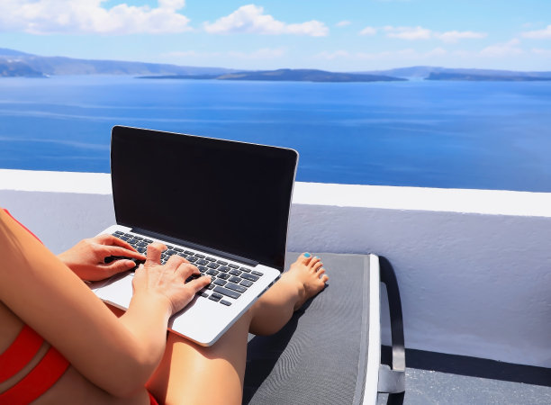 游牧数字与笔记本电脑和远程运行与地中海和圣托里尼火山口明亮的风景-工作度假的概念图片下载