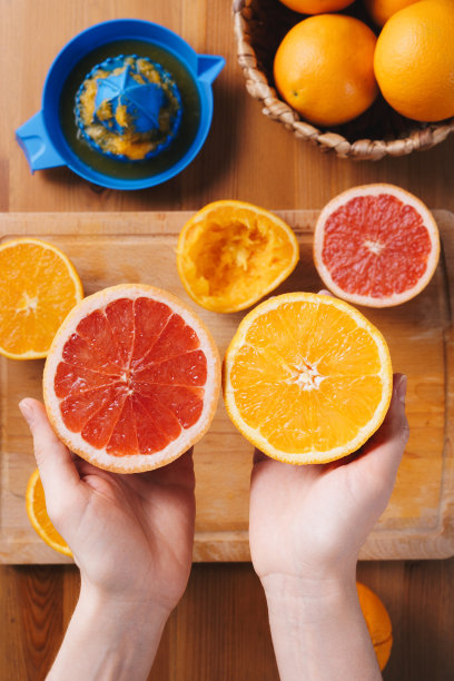 手拿着切好的橘子和葡萄柚放在木制砧板上，桌面视图图片下载