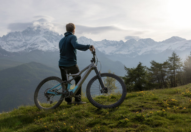 一个年轻人骑着电动自行车停在山间草地上图片下载