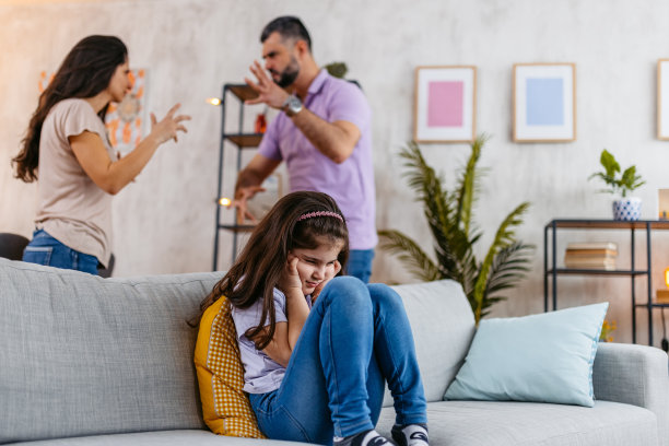 小女孩捂着耳朵，她的父母在她身后争吵图片下载