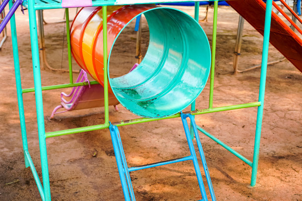 图为公共操场上用废弃油桶制作滑梯和隧道的儿童游乐设备。图片下载