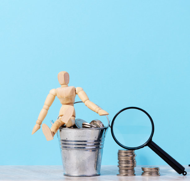 一个木制的人体模型和硬币放在一个蓝色背景的小桶里，一个高收入的概念，补贴图片下载