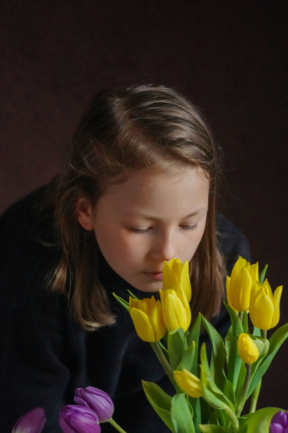 漂亮的长发女孩在黑暗的背景弯下腰，黄色和紫色的郁金香，工作室拍摄的深色。图片下载