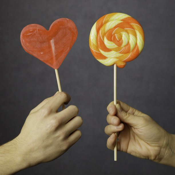 手里拿着红色和黄色/橙色的彩色棒棒糖图片下载