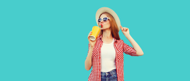 年轻女子的肖像喝鲜果汁戴夏季草帽，格子衬衫孤立在蓝色背景图片下载