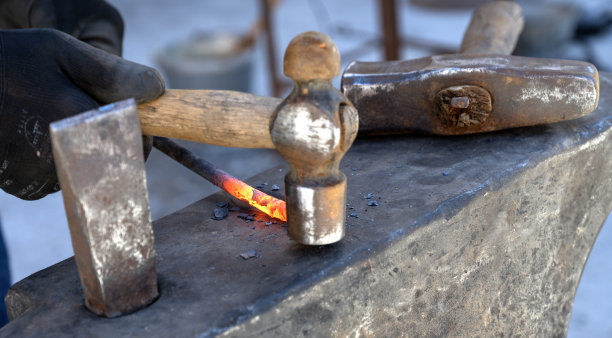 用锤子把热金属锻造成一把刀——用钳子夹住刀图片下载