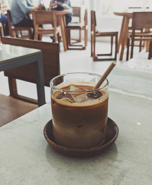 在咖啡馆里，背景模糊的玻璃杯里装着咖啡的人像照片图片下载